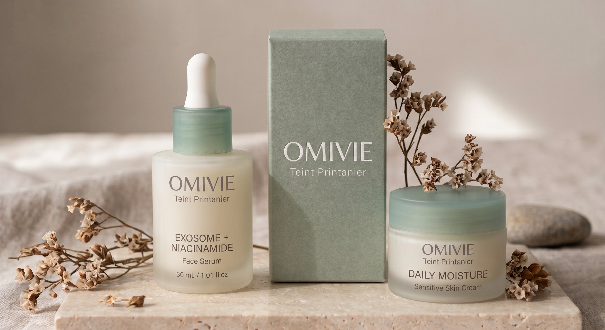 Omivie Teint Printanier packaging concept: Exosome + Niacinamide Face Serum and Daily Moisture Sensitive Skin Cream beside a sage-green box on pale stone.